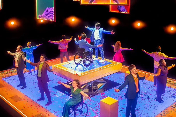 A photo showing a group of performers waving their hands on a brightly lit stage surrounded by darkness 