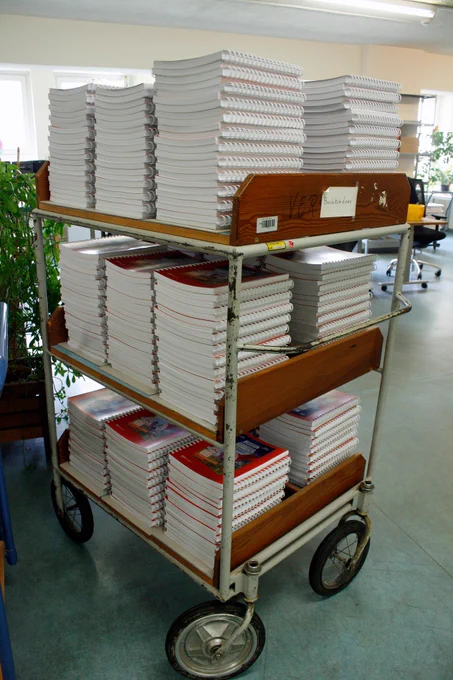 Ein Bücherwagen mit drei Etagen, auf denen viele Stapel von Büchern liegen und auf den Versand warten.
