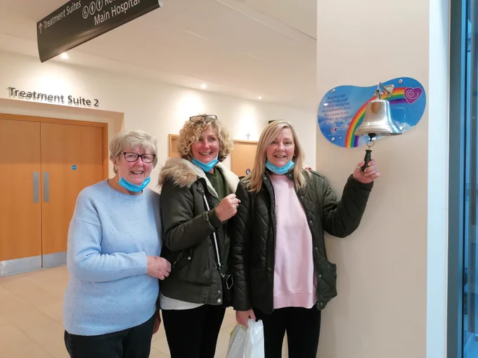 Three woman in hospital corridor. One woman is ringing a bell