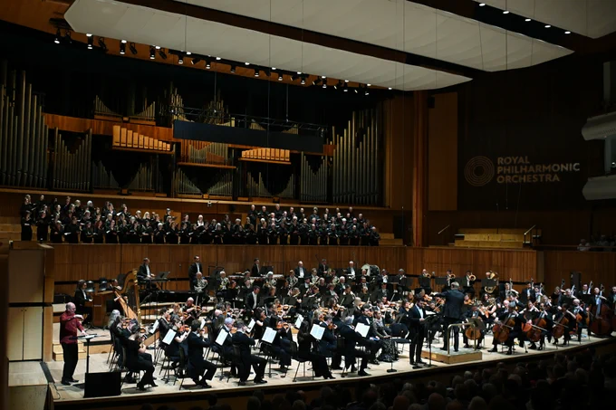 The Orchestra performing on stage in the Royal Festival Hall with the Philharmonia Chorus in the choir stalls, BSL artist Paul Whittaker signing on stage right and tenor Pavel Petrov at the front and centre.