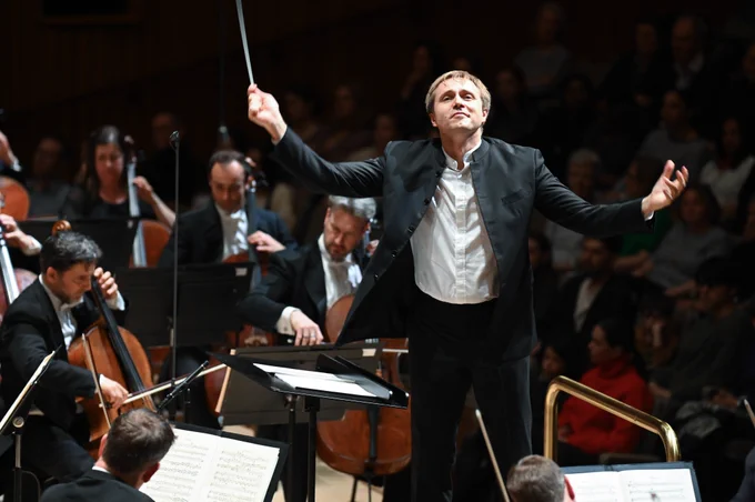 Vasily Petrenko with both arms raised and smiling as he conducts.