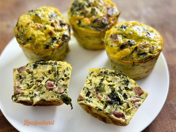 Close up of three whole Eggs Florentine Ham & Cheese cups and one split in half on a white plate. 