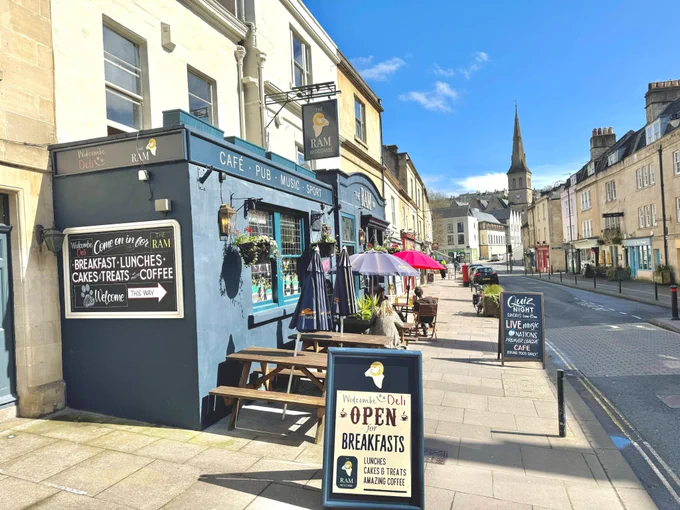 External image of The Ram in Widcombe, Bath (now incorporating Widcombe Deli) with blue skies, featuring a traffic-free Widcombe Parade, at the end of which lies The Apartment, Bath.