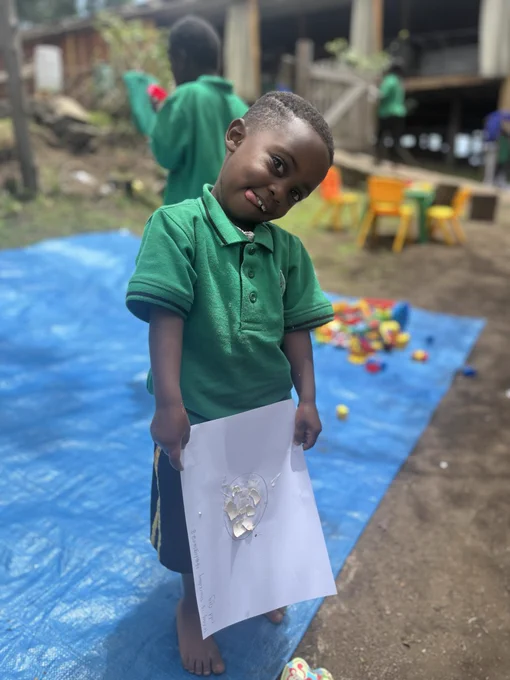 Kyaninga Inclusive Model School student smiles and holds up a piece of paper displaying their 'odd egg,' crafted from eggshells and glue.