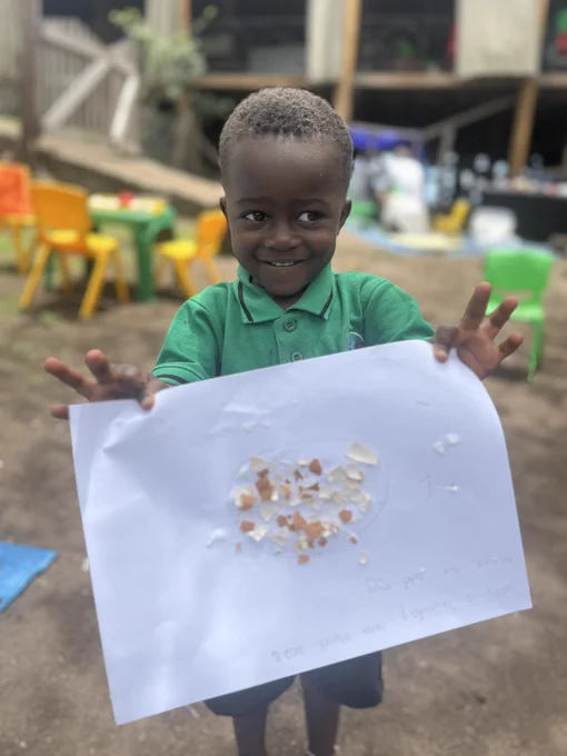 Kyaninga Inclusive Model School student smiles and holds up a piece of paper displaying their 'odd egg,' crafted from eggshells and glue.