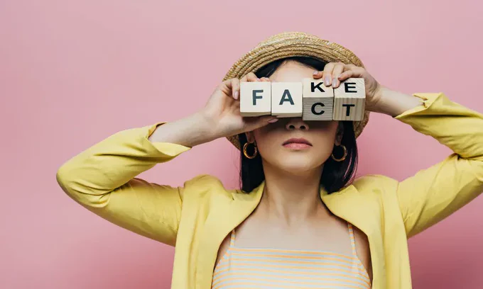 Femme tenant des cubes en bois devant le visage avec des lettres fausses et factuelles isolées sur du rose