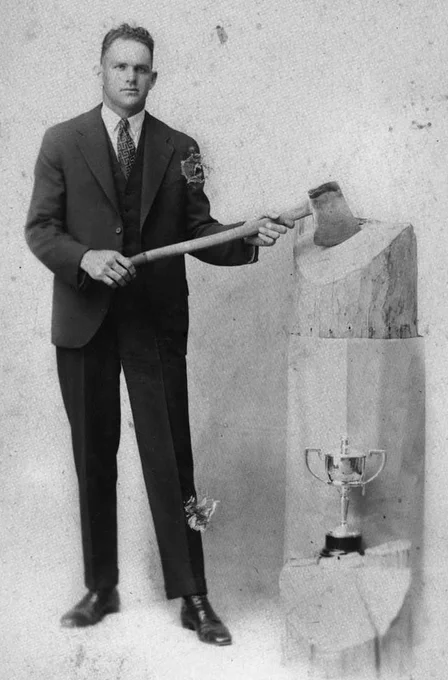 Grayscale photograph of a man in a suit holding an axe, chopping into wood.
