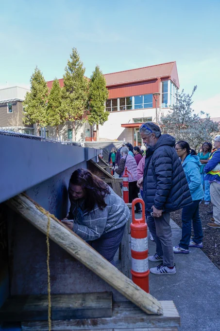 A group of people signs a steel beam. 