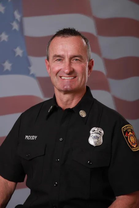 Formal Los Angeles Fire Department Portrait Photograph of LAFD Captain Richard Moody, smiling in his work uniform with badge, with a U.S. Flag motif in the background. 