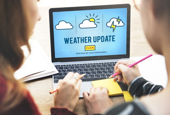 Two individuals at a laptop checking on weather updates. 