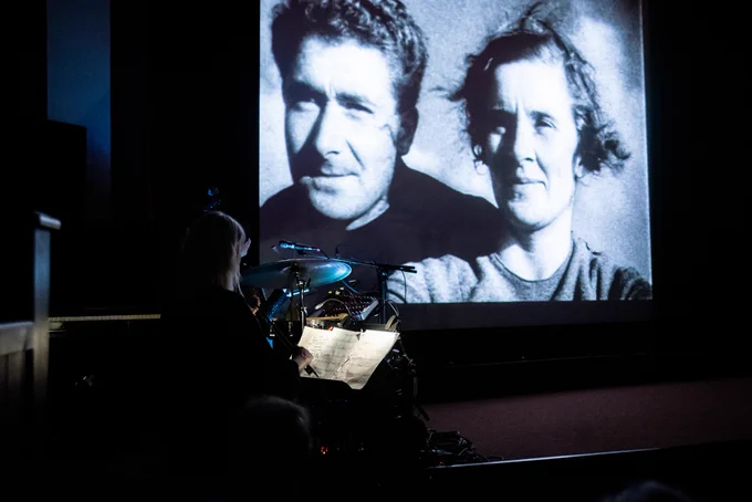 Characters Johnny and Enga are visible on the big screen with dimly illuminated musicians visible in the foreground.
