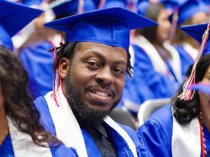 A male graduate is found in the midst of the class of 2023 crowd; he is smiling at the camera