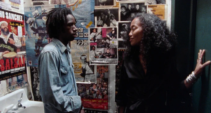 Actors Saul Williams and Sonja Sohn talking in a bathroom that is decorated with posters.