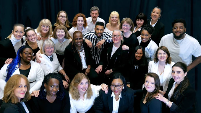A group of people in black and white clothing stand in a group, looking up at the camera. 