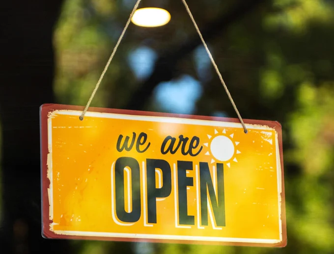 A yellow sign in a shop window with the words 'we are open' on it 