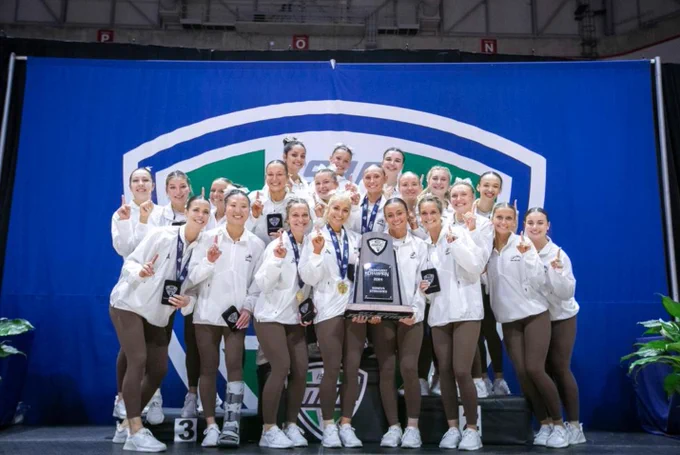 A team photo of Western's Gymnastics team holding their new MAC trophy and medals. 