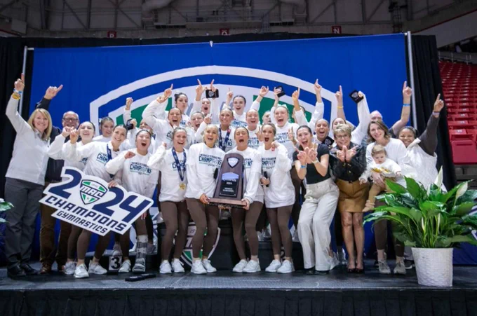 A team photo of the Gymnasts and the coaches holding the trophy and a champions banner. 