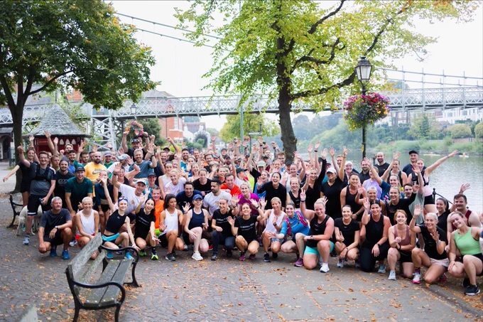 Large group of people wearing running gear and sitting next to a river and bridge