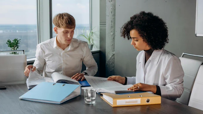 Man and woman at boardroom table examining files. 