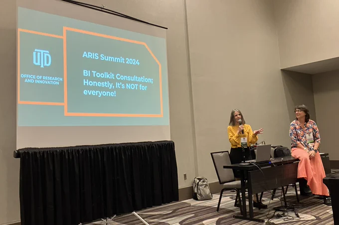 Two women stand next to a screen showing the title of their talk: ARIS Summit 2024: BI Toolkit Consultation; Honestly, it’s NOT for everyone.