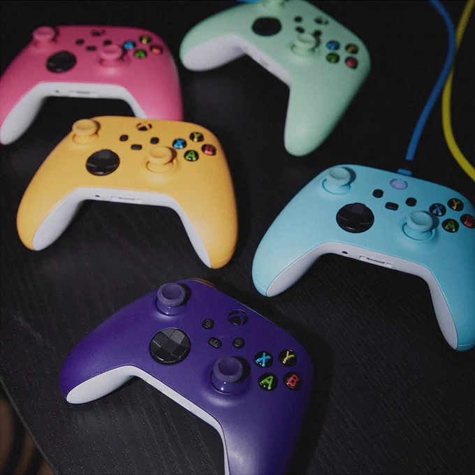 Five game controllers on a dark table different colours.
