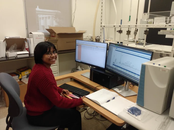 Woman sits at a computer controlling a mass spectrometer, newly unpacked from boxes, with her first data on the screen and smiles.