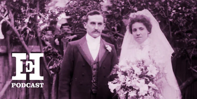 A purple-tinted photo of a couple on their wedding day. The woman is on the right wearing a tradtional veil and dress and holding a big bouquet, and a man in a smart suit stands on her left. They are posing in front of a garden scene.