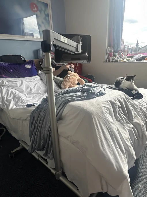 A bed with a stand which has a tobii dynavox eye gaze device mounted on it which is above the bed.