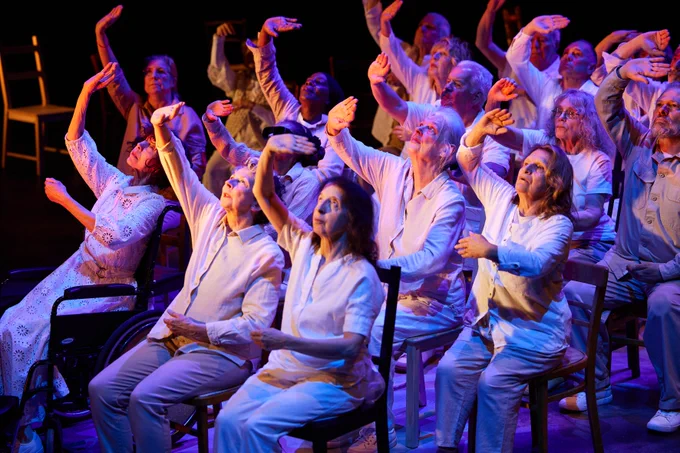 People sat on chairs and lit by a blue light. They all have one arm raised up.