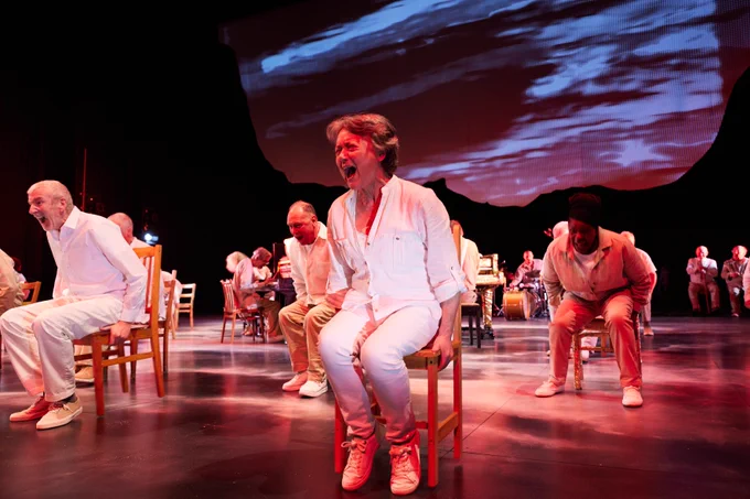 Some people on stage sat on chairs. They are wearing white clothes and are shouting.