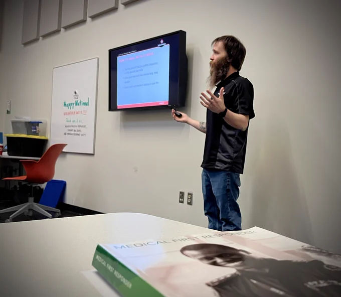 St. John Ambulance Instructor leading a Medical First Responder (MFR) course in a classroom, with the MFR textbook in the foreground.