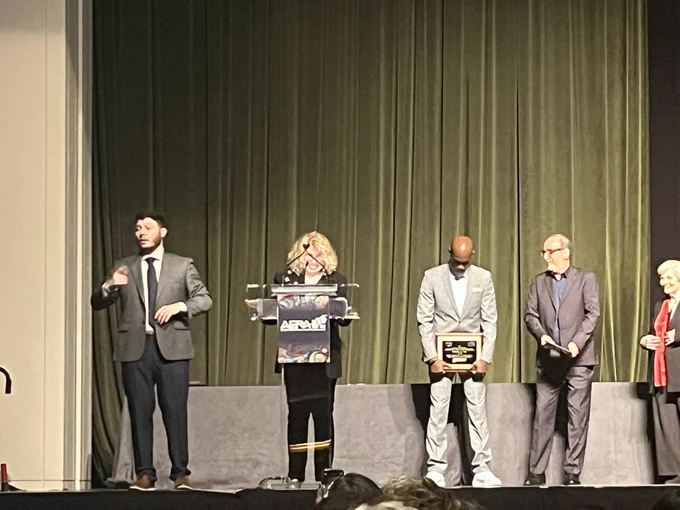 Kris Gutiérrez stands on stage smiling. She is on stage with other people to the right and left of her.