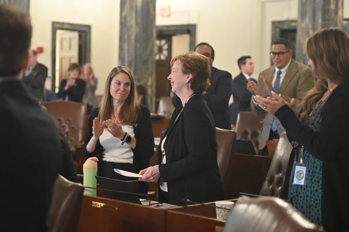 Senator Gillespie smiles while Senators surrounding her give her a round of applause.
