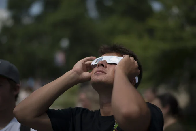 A young man looking up at solar eclipse wearing paper protective glasses.