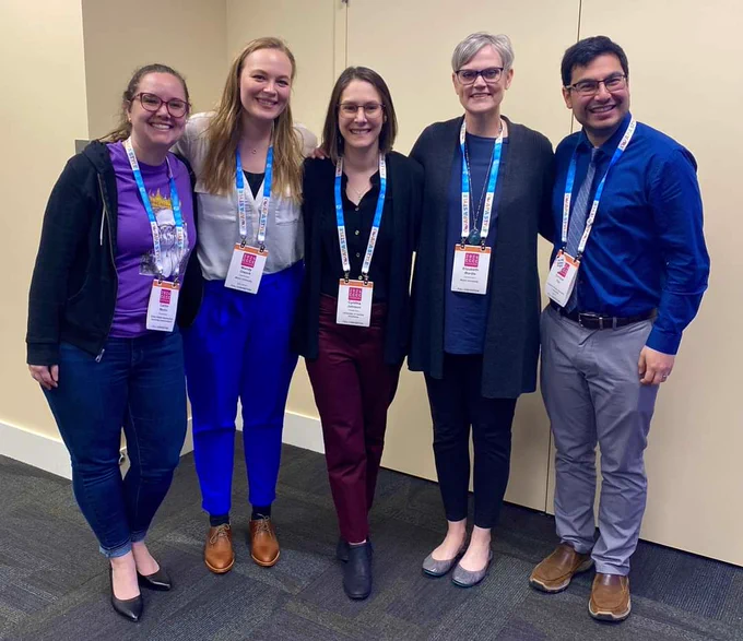 Five people with conference lanyards lined up smiling at the camera. 