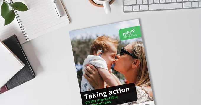 Cover of the 'Taking action on the preventable burden of mito' report on a white desk with notebooks and a keyboard. 