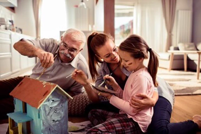 A family sit together painting a small wooden house.