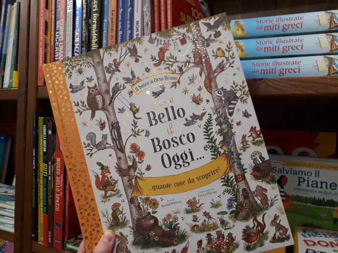 The book is 'Com'è Bello il Bosco Oggi', by Rachel Piercey and Freya Hartas, held up against a shelf of children's books.
