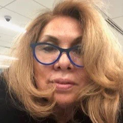 Kris Gutierrez looks at the camera. She is wearing blue glasses.
