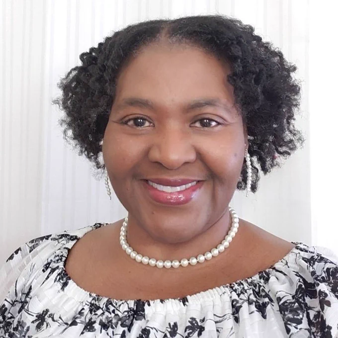 Felicia Moore Mensah smiles at the camera. She is wearing a black and white floral shirt and pearl earrings and necklace.