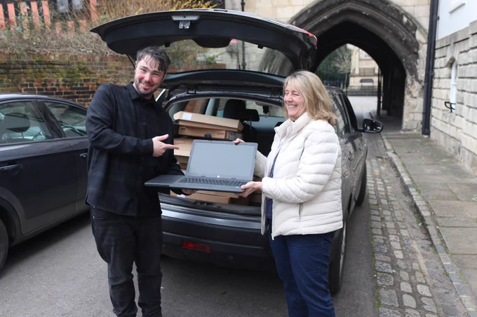 GRCC's Daniel Gale stands outside of Community House, smiling and pointing at a laptop he holds with Jenny Evans of The ITSA Digital Trust. 