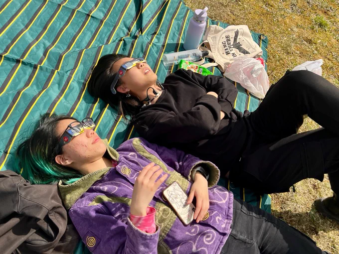 Two young women lay on a blanket in the grass to watch the total eclipse.