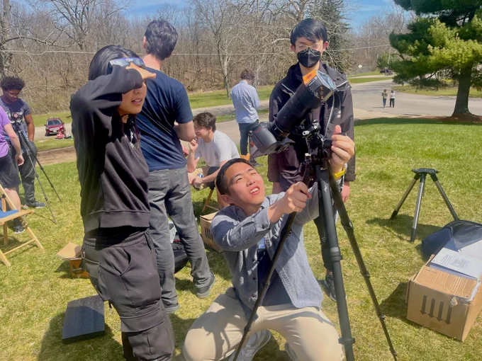 One student sets up a camera to capture the total eclipse while two other students watch.