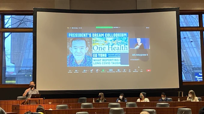 Photo from long COVID community roundtable event, with science journalist Ed Yong.  Ed Yong is speaking presenting in front of a Zoom presentation with slides on his long COVID reporting. Other speakers and roundtable members are seated beside Ed.