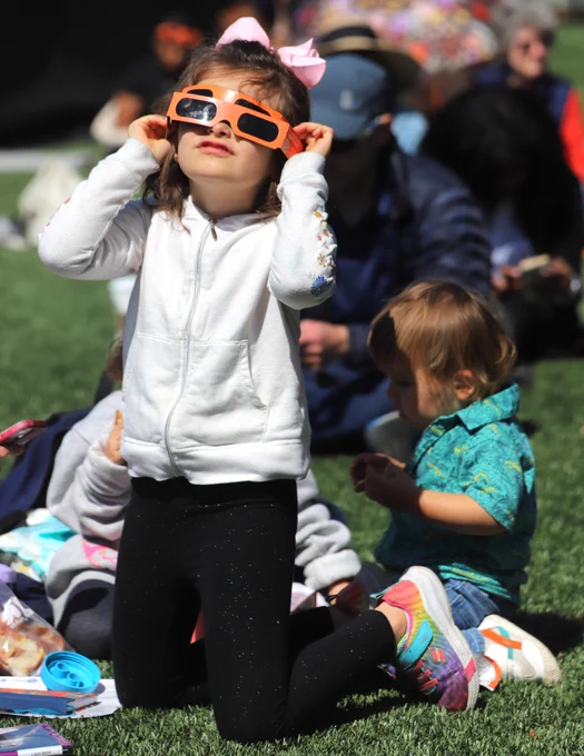 A young child watches the eclipse with two pair of orange Caltech viewing glasses