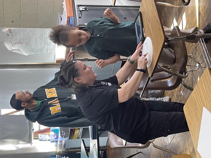 A teacher working with a student, drawing on a paper plate to represent the 2024 solar eclipse 