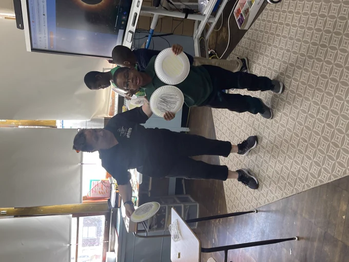 A student stands next to his teacher presenting his paper plates he has colored to represent the 2024 solar eclipse 