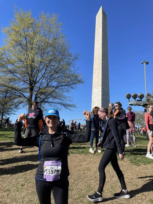 Secretary Haaland throws her arms up in front of the Washington monument, wearing her runners bib.