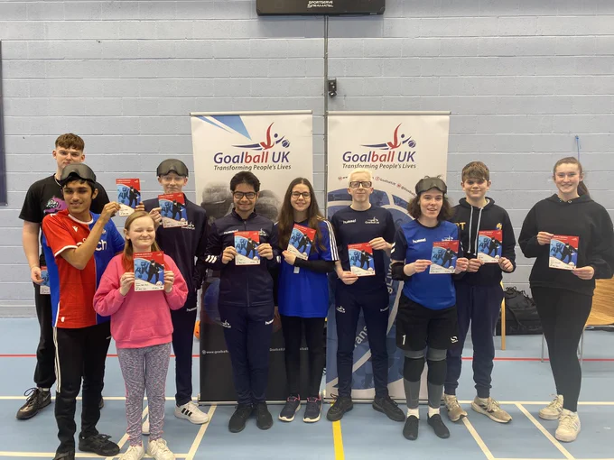 A group of young people stand holding their certificates in a sports hall