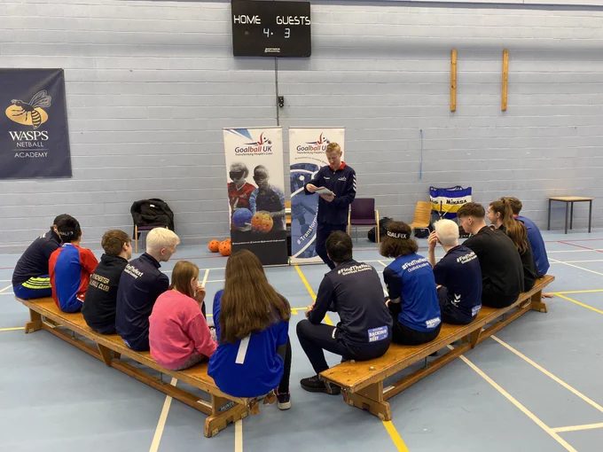 Stephen Newey talks to a group of young people who are sat on benches facing him
